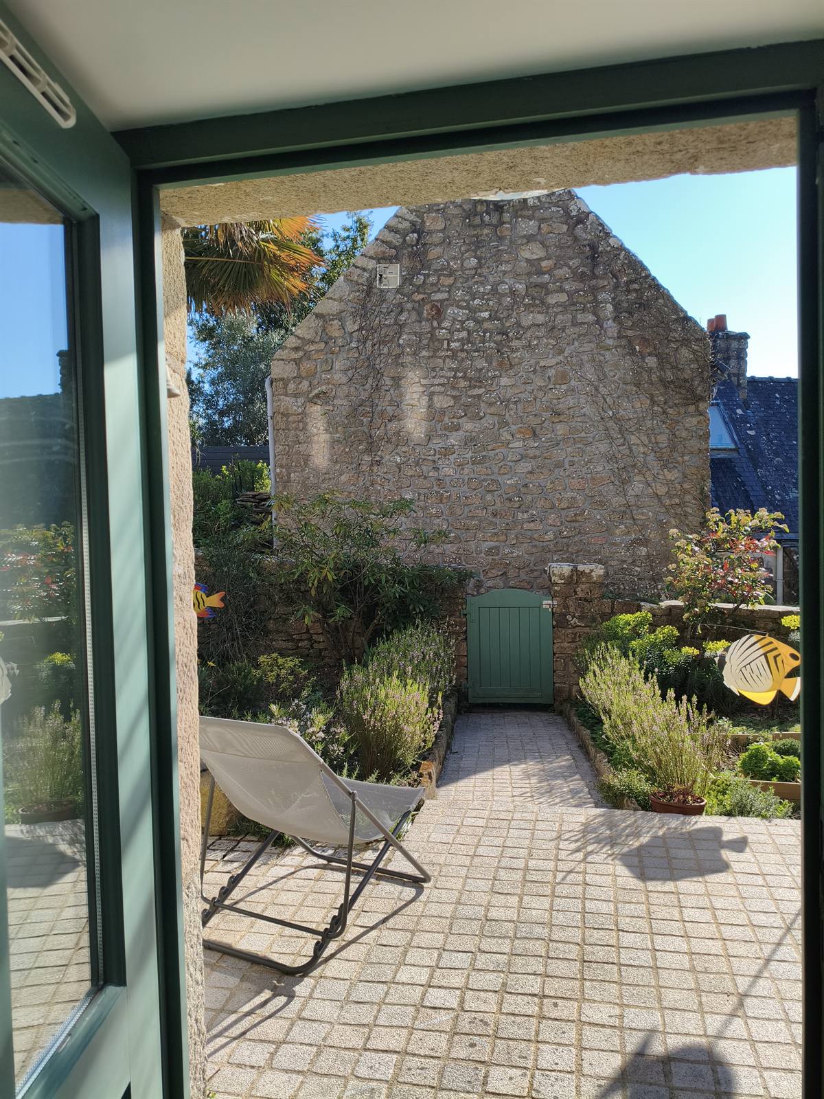Porte-fenêtre ouverte sur la cour pavée et le jardin de la maison