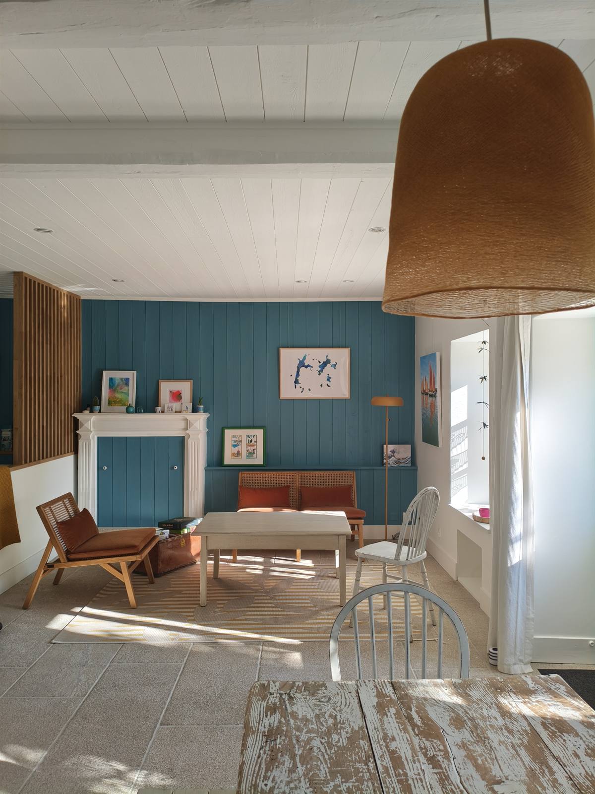 La pièce de vie sous la suspension en fibre naturelle, table en bois patiné au premier plan