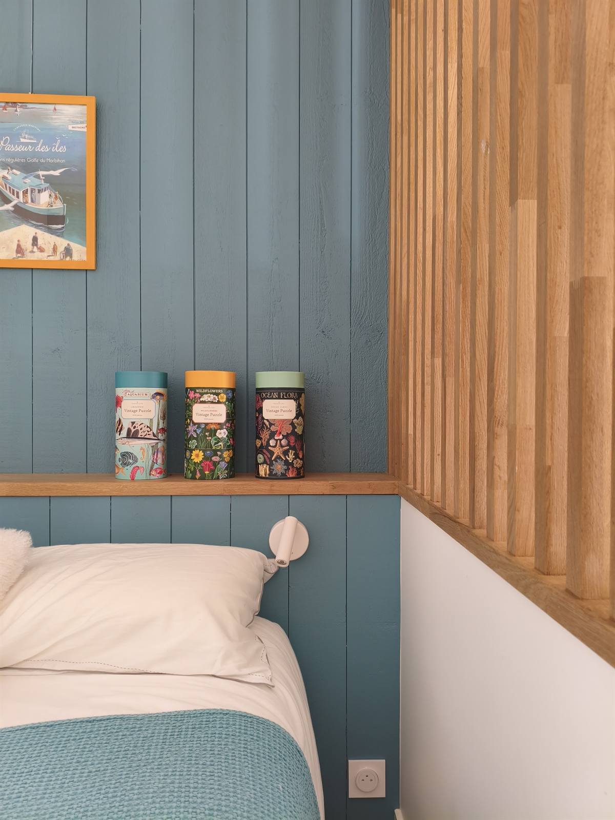 Étagère en bois au-dessus du lit et liseuse murale sur le lambris bleu canard