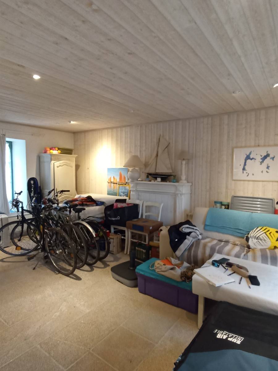 Avant : pièce encombrée de vélos et de bagages, lambris clair et cheminée blanche