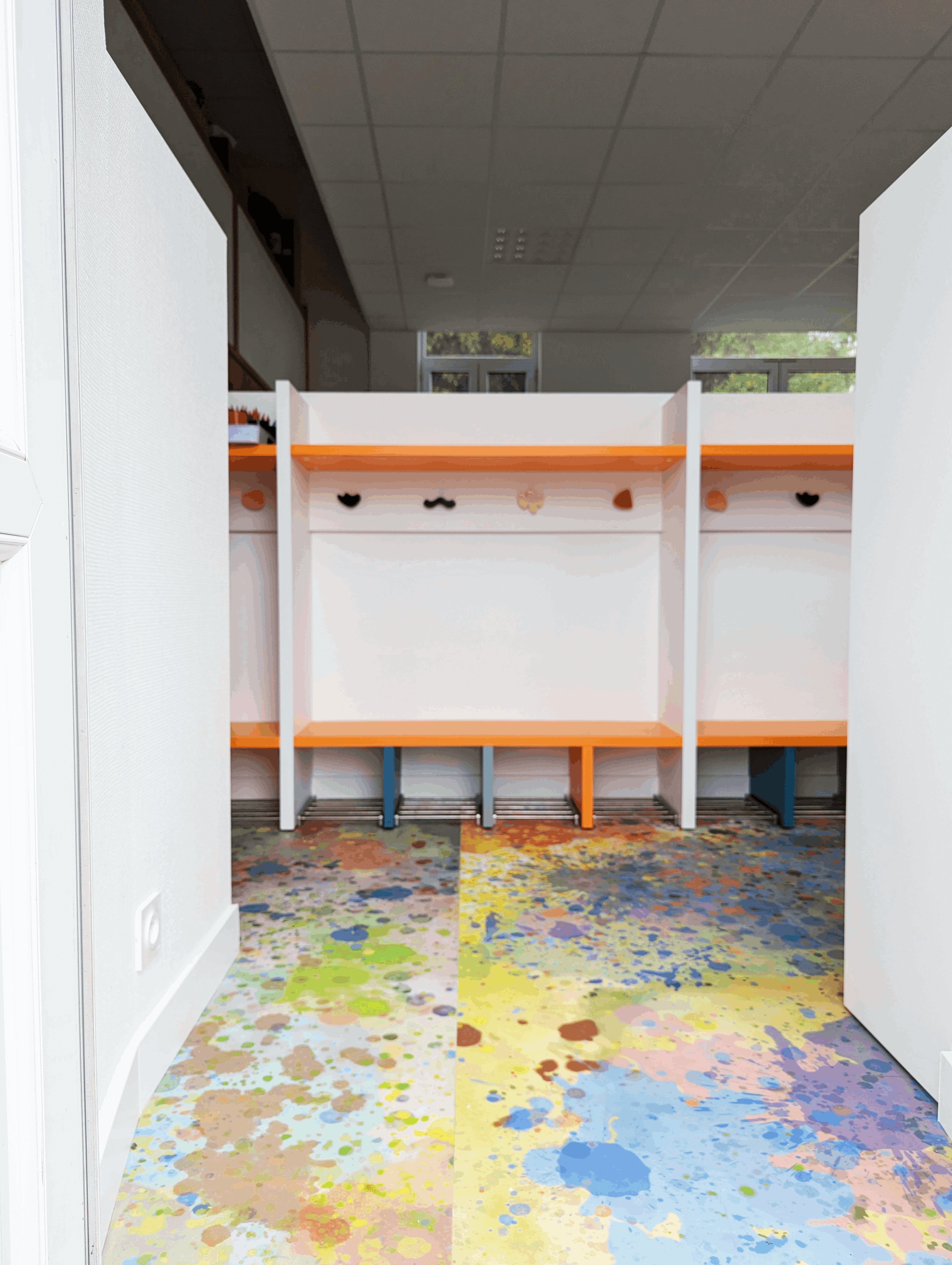 Vestiaire de maternelle : casiers blancs et bancs orange, patères ludiques et sol souple coloré