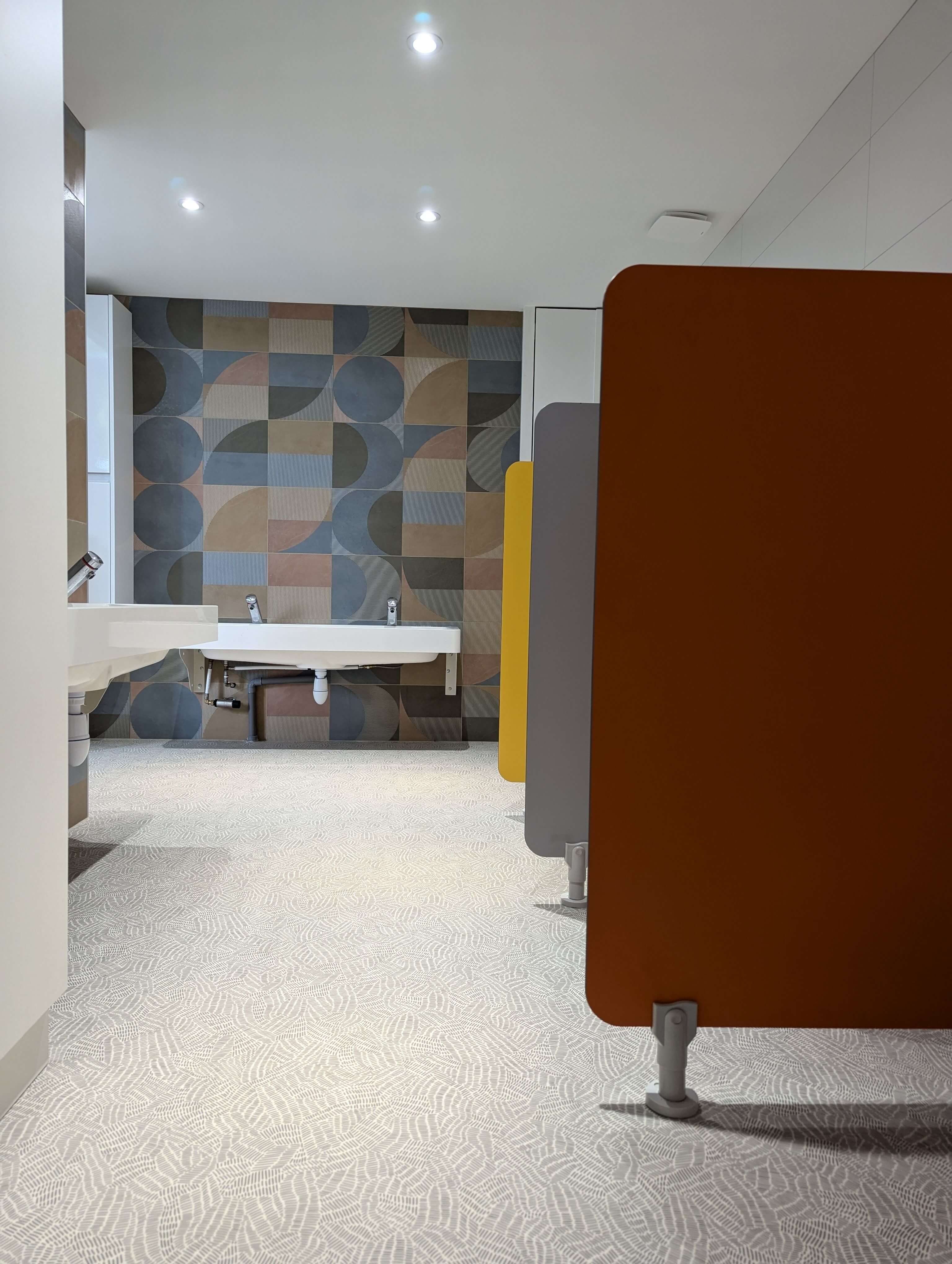 Cabines de WC à cloisons colorées terracotta, jaune et grise dans les sanitaires rénovés