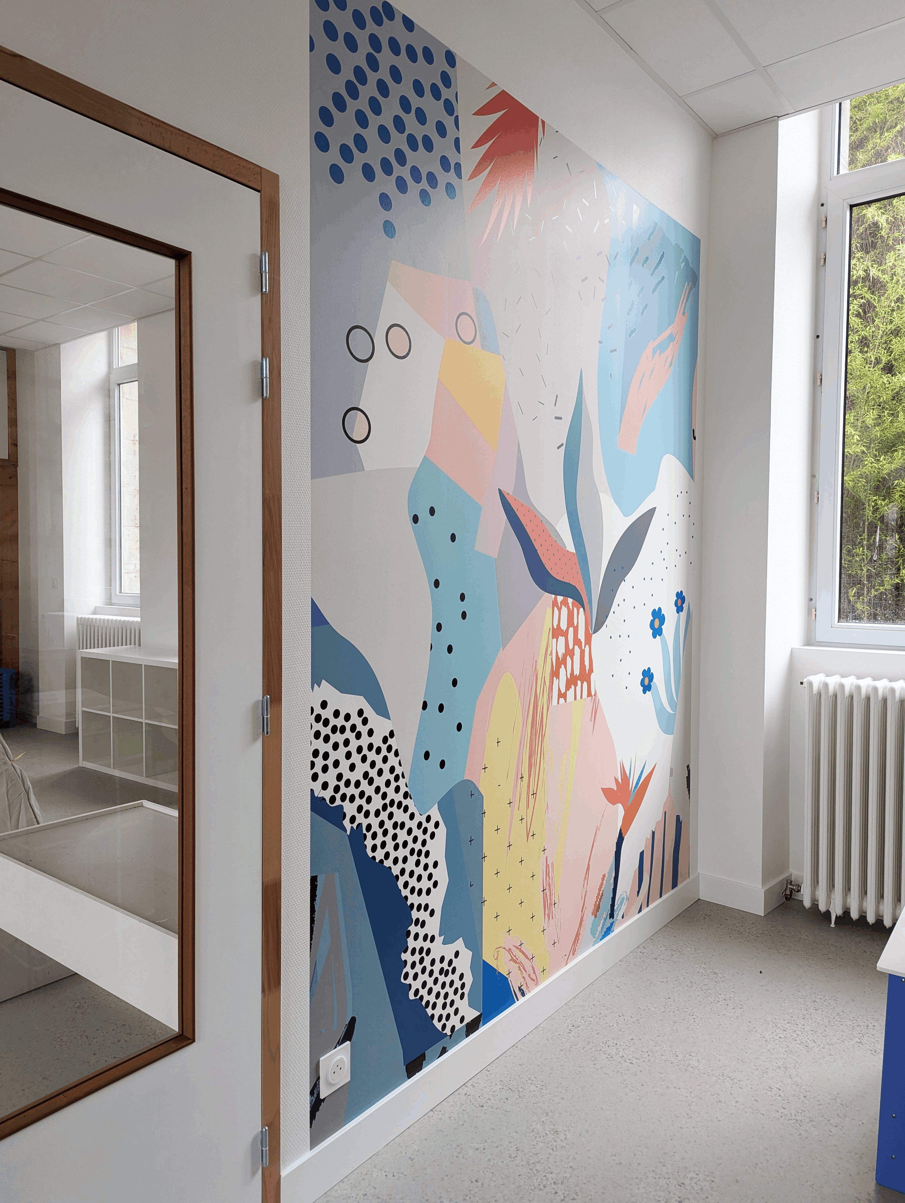 Classe de maternelle : fresque murale colorée aux formes abstraites, près de la fenêtre