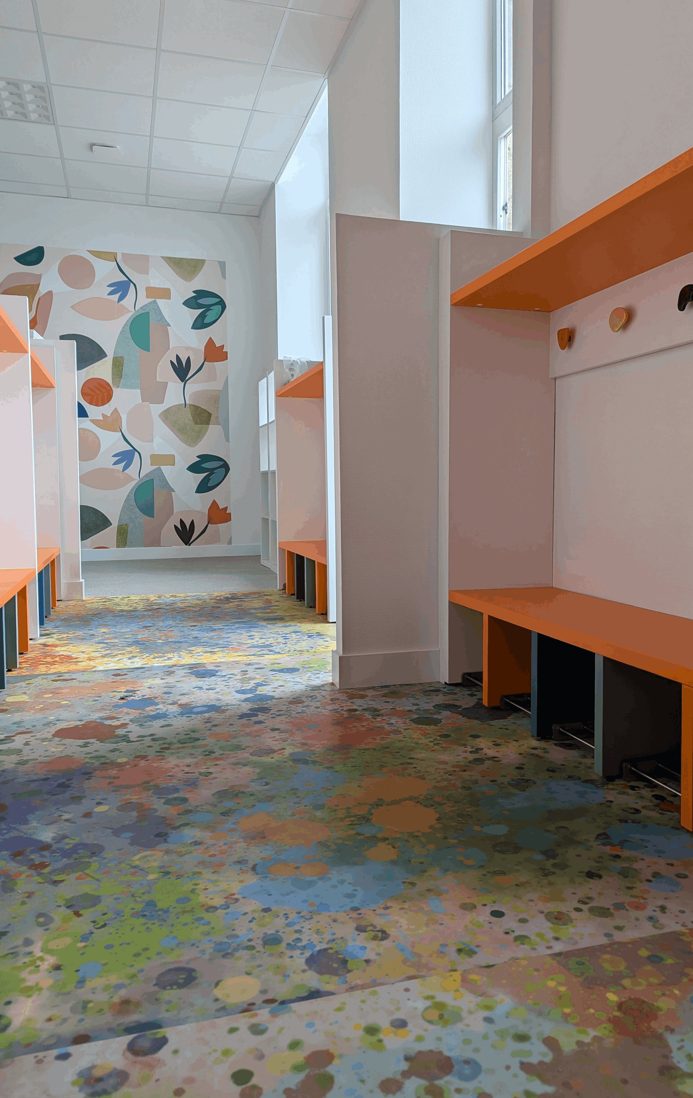 Rangée de vestiaires orange et papier peint panoramique végétal au fond du couloir de la maternelle