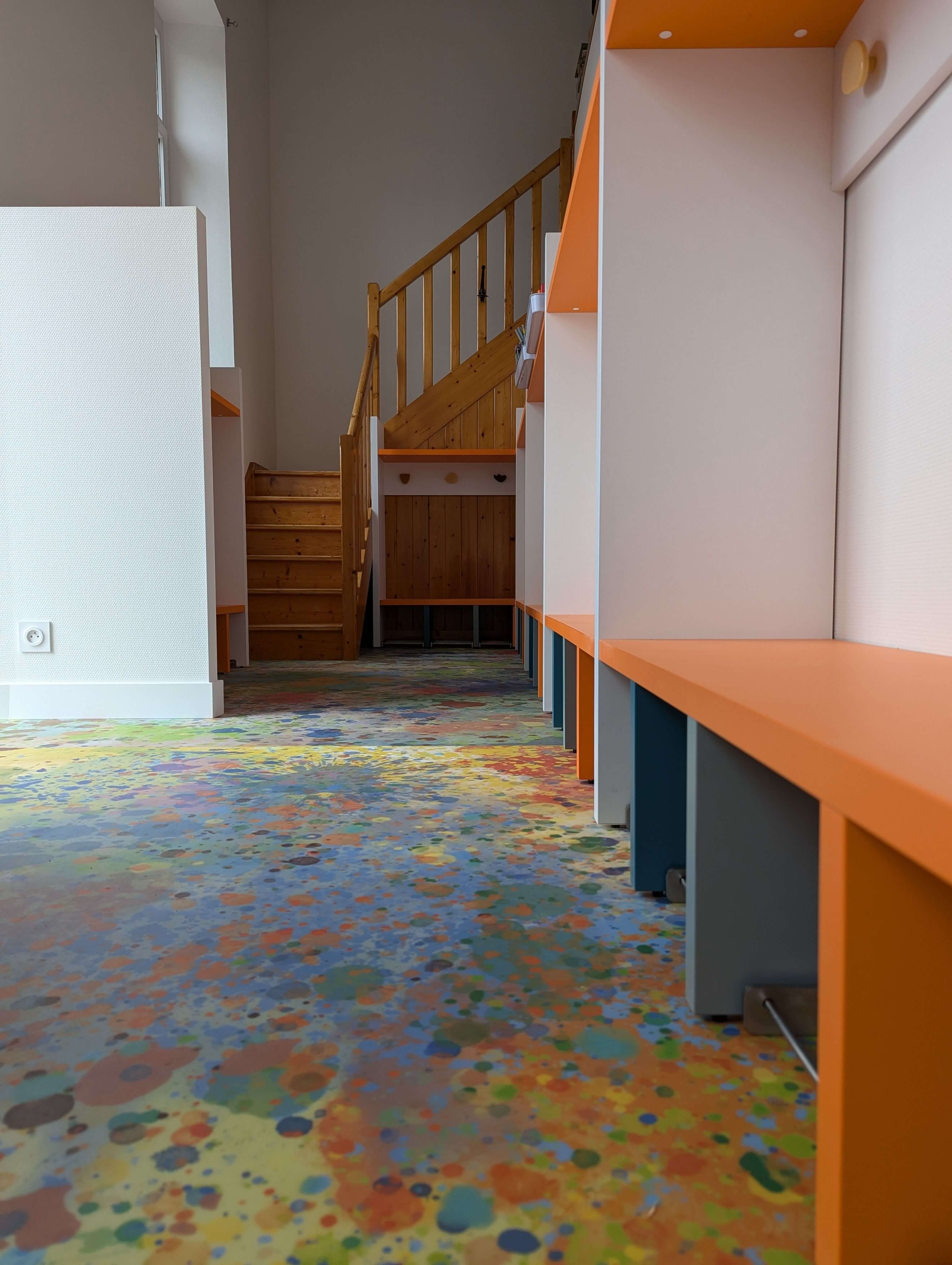 Circulation du vestiaire : bancs orange en enfilade et sol souple à motif d'éclaboussures