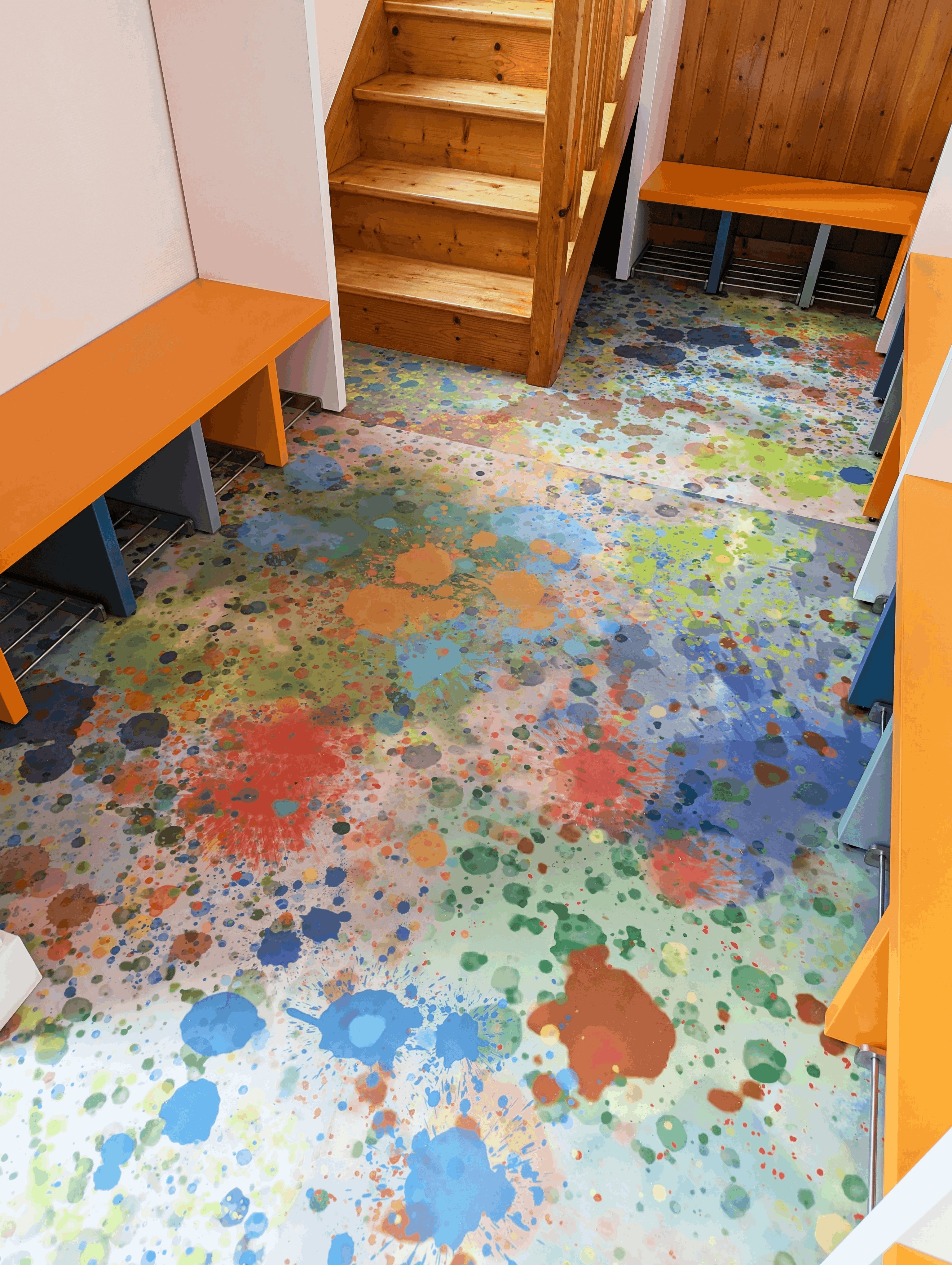 Vue plongeante sur le sol souple coloré du vestiaire et l'escalier en bois de l'école