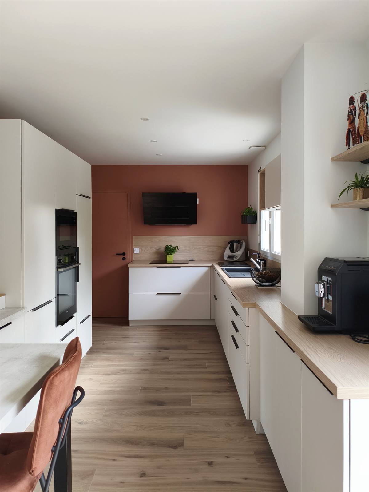 Cuisine blanche en U, plan de travail effet bois et mur terracotta au fond