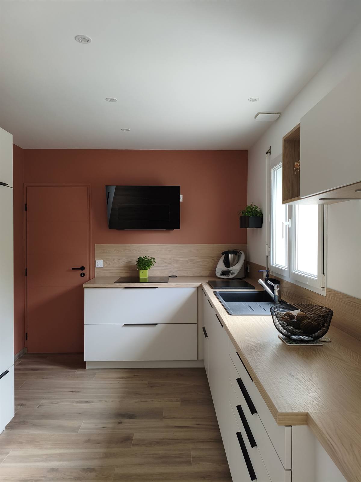 La cuisine vue depuis l'entrée : meubles blancs, plan de travail effet bois et fenêtre