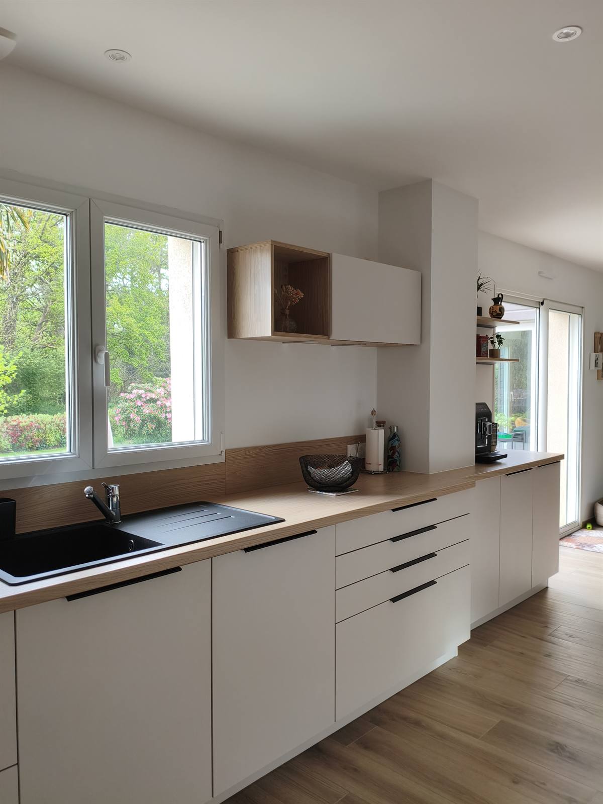 Évier noir sous la fenêtre, meubles blancs à tiroirs et niche en bois suspendue