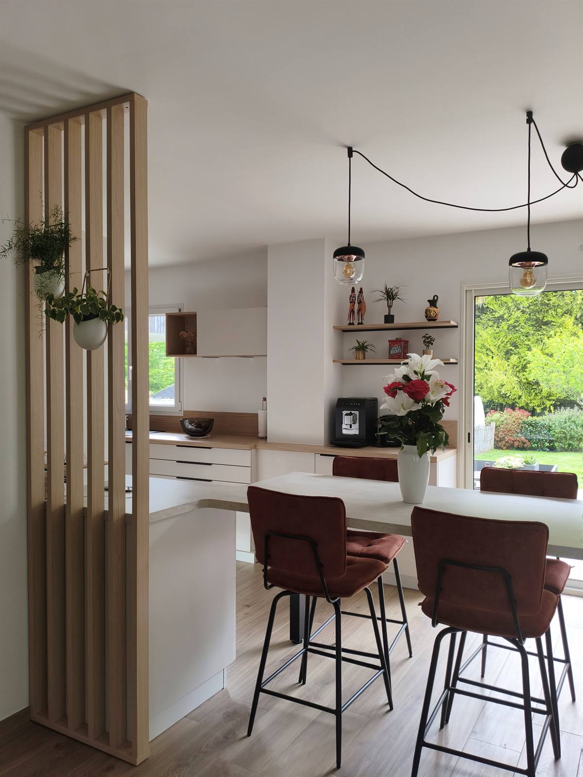 Le claustra en bois et ses plantes suspendues, la baie vitrée sur le jardin au fond