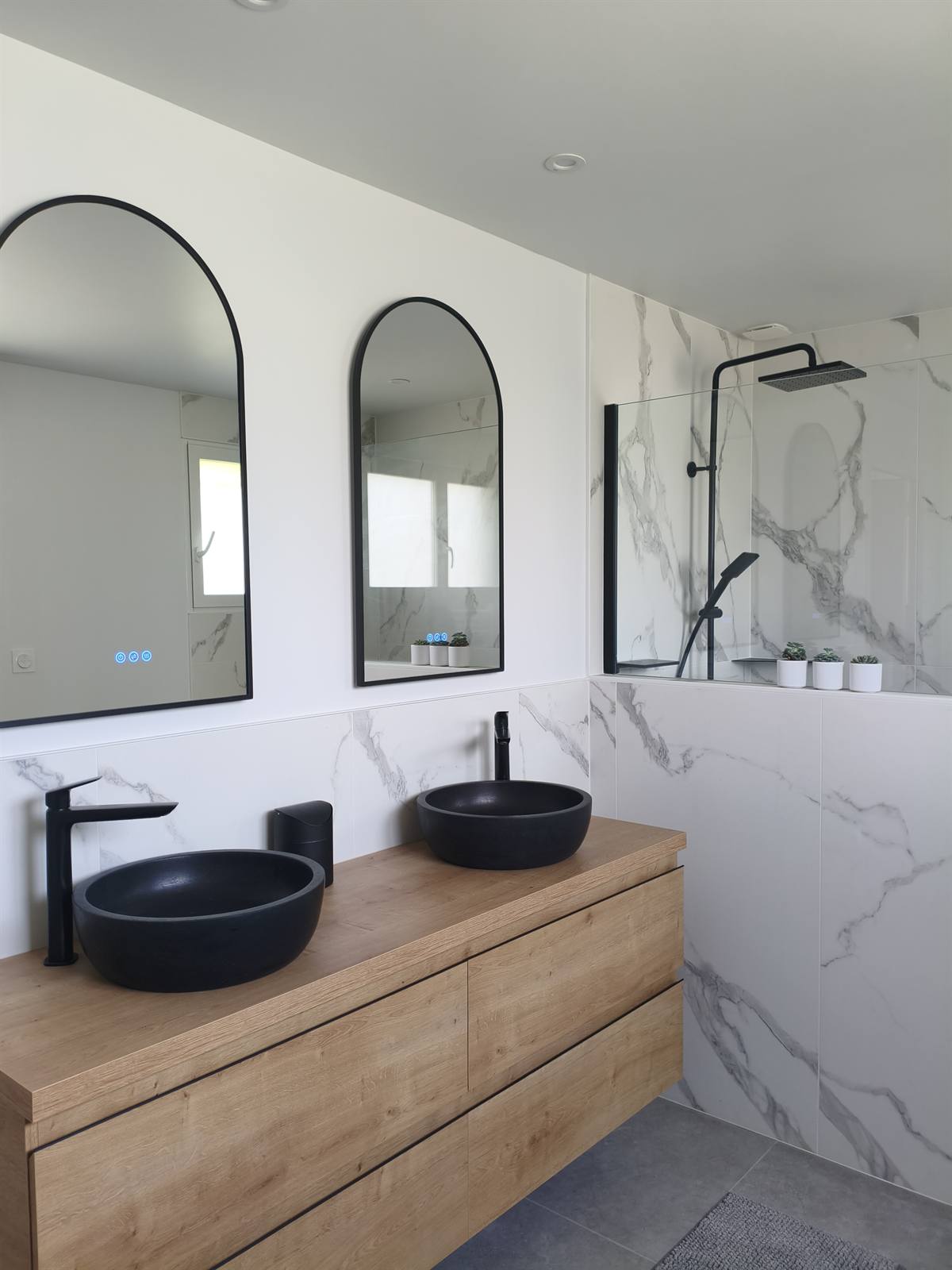 Double vasque noire sur meuble en chêne, miroirs en arche et douche à l'italienne en faïence effet marbre