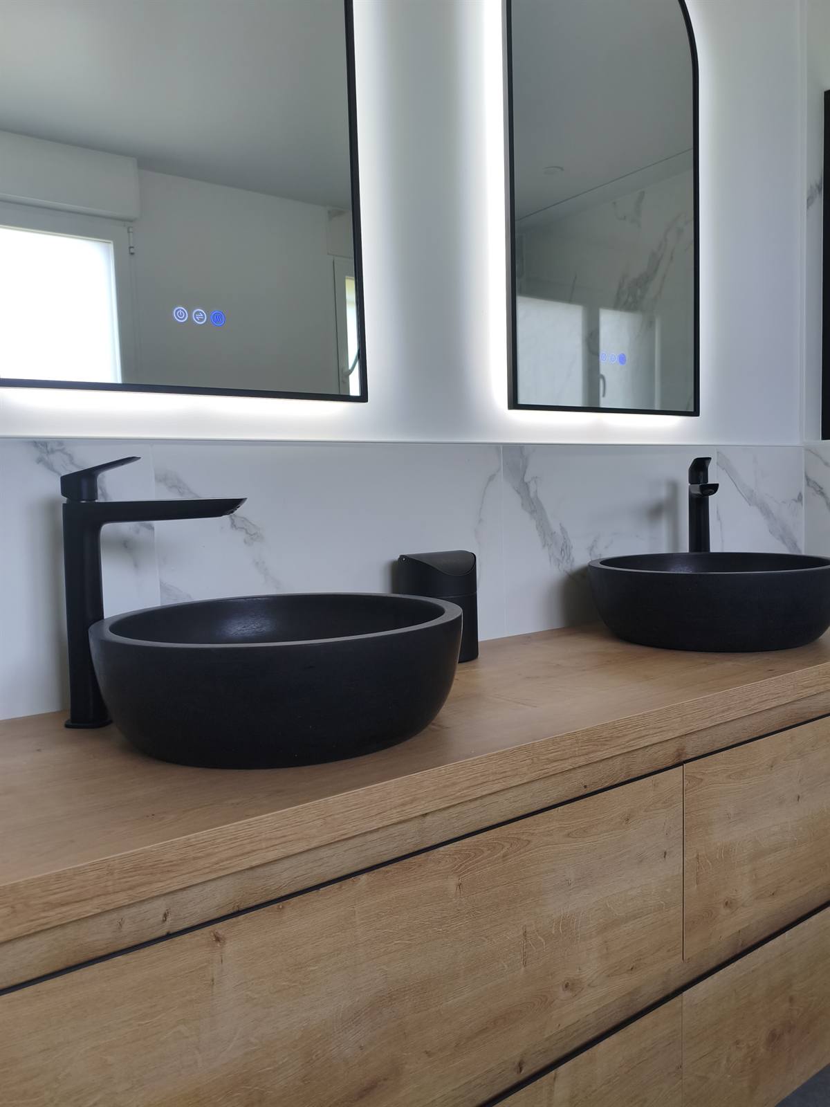 Miroirs rétroéclairés au-dessus des deux vasques noires posées sur le plan en chêne