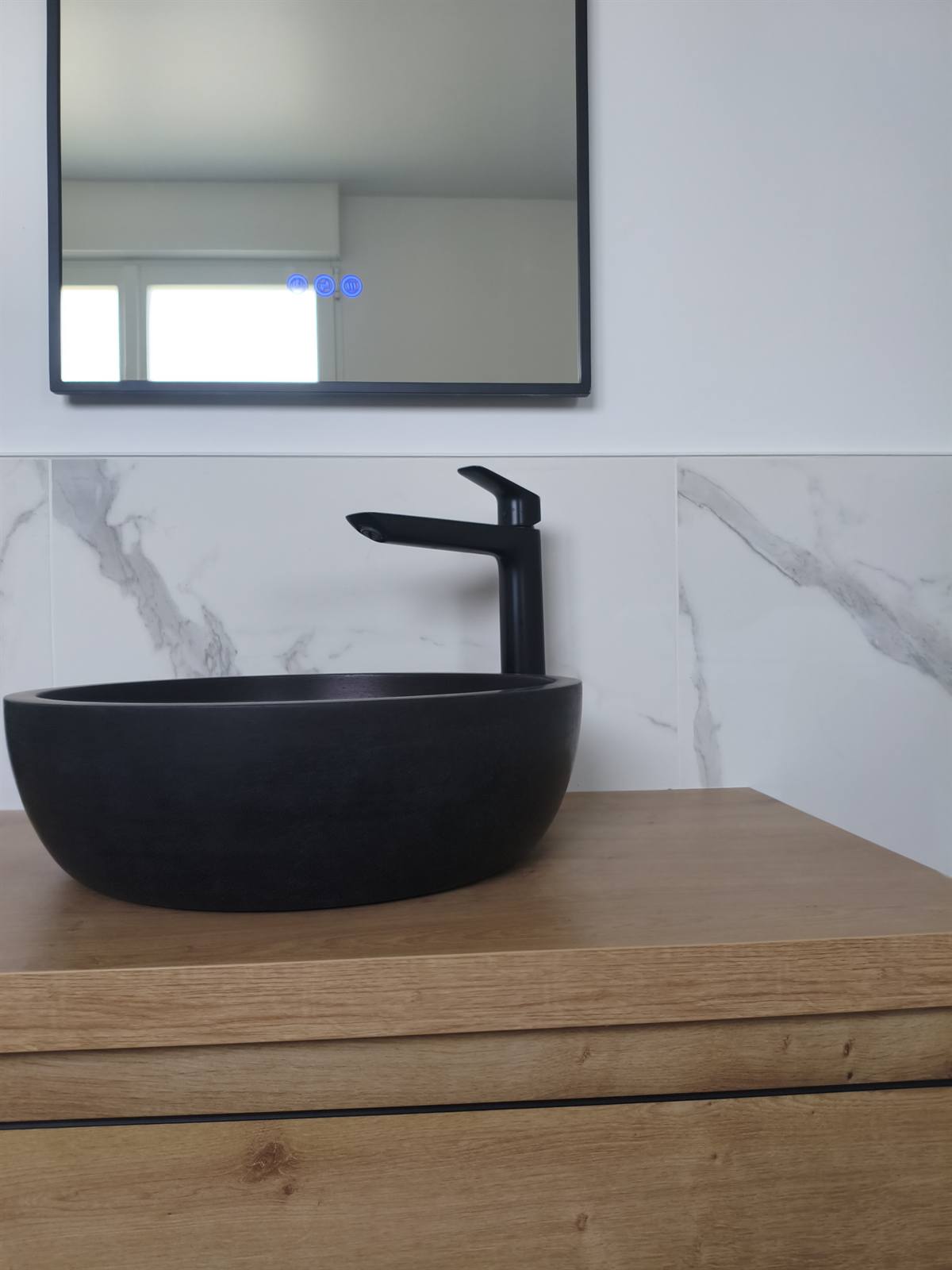 Détail d'une vasque ronde noire et de son mitigeur noir mat sur le meuble en chêne