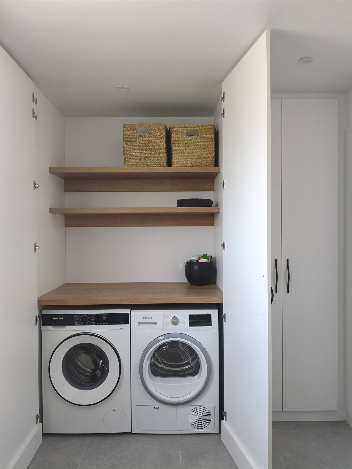 Buanderie intégrée à la salle de bain : lave-linge et sèche-linge sous un plan en chêne, étagères et paniers