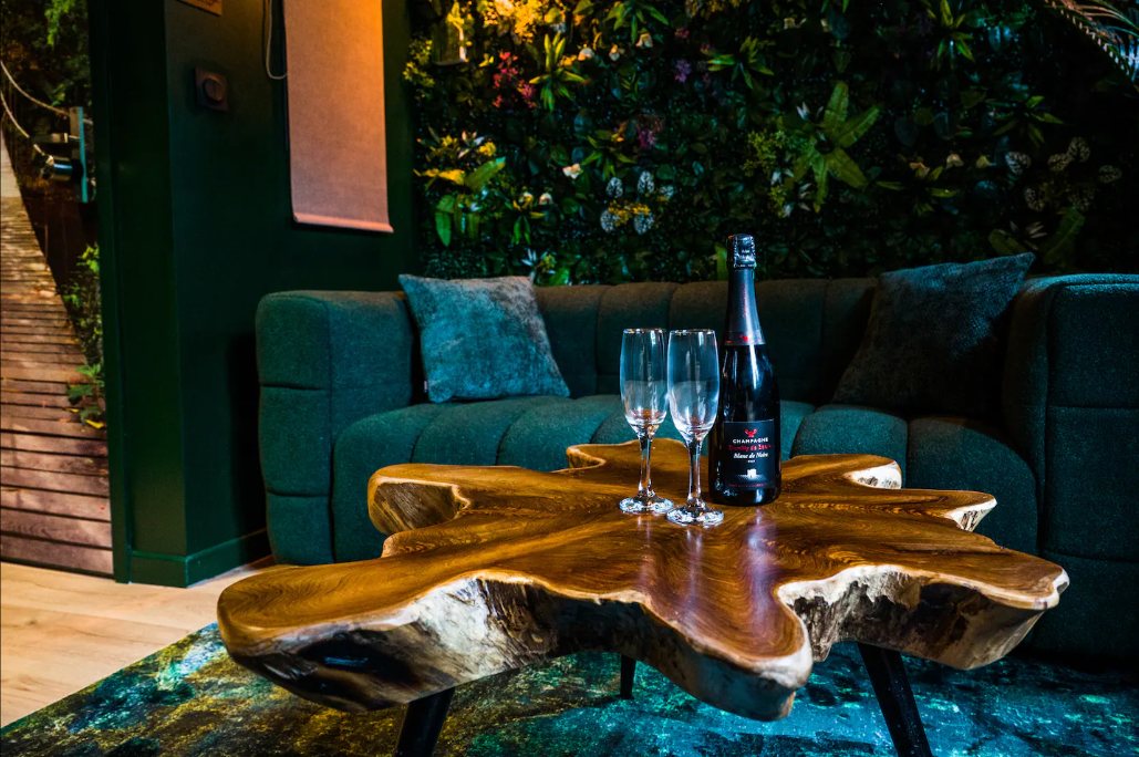 Salon : canapé vert sapin, table basse en tranche de bois brut et mur végétal