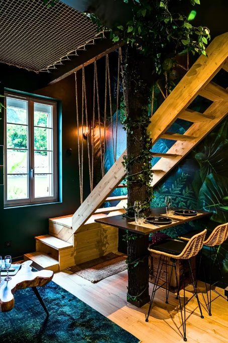 Escalier en bois clair vers la mezzanine, tronc d'arbre habillé de lierre, table haute et filet suspendu au plafond