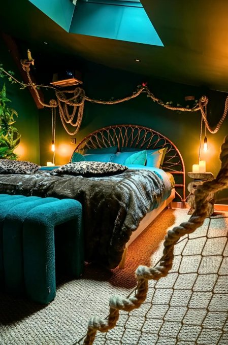 Chambre aux murs vert foncé : tête de lit en rotin, lianes de corde et appliques à ampoule