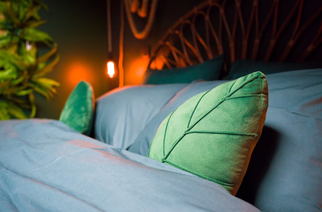 Détail du lit : coussin en velours vert en forme de feuille devant la tête de lit en rotin