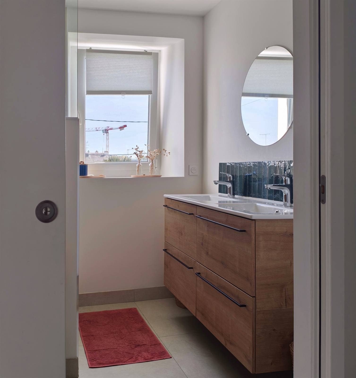Salle de bains rénovée : meuble double vasque en chêne et zellige bleu canard sous la fenêtre