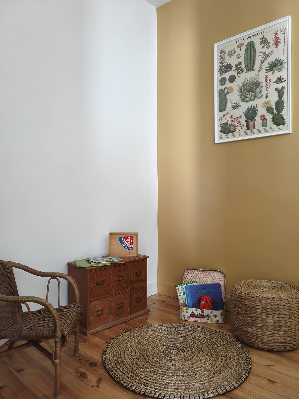 Coin des petits-enfants : mur ocre, fauteuil en rotin, tapis en jute et paniers