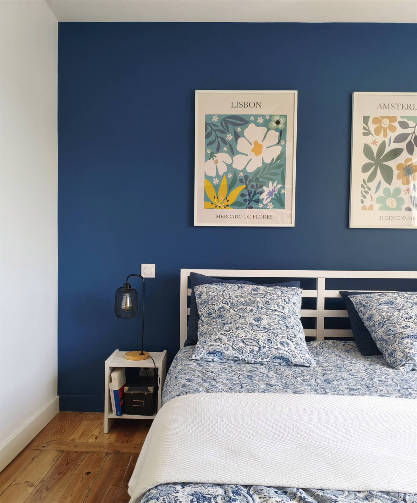 Le lit devant le mur bleu nuit, affiches botaniques et chevet blanc