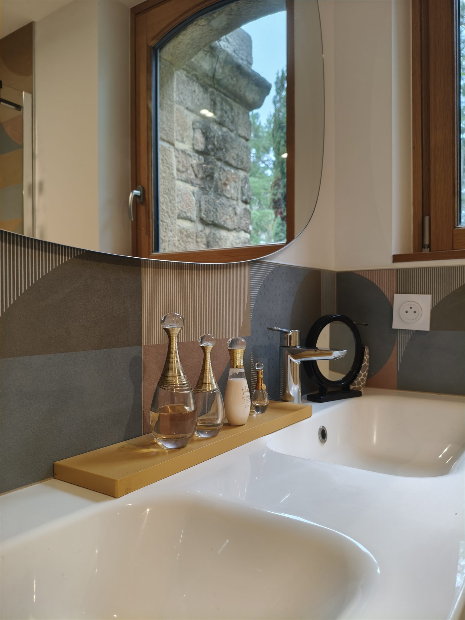 Double vasque blanche, miroir aux formes arrondies et fenêtre cintrée donnant sur les arbres
