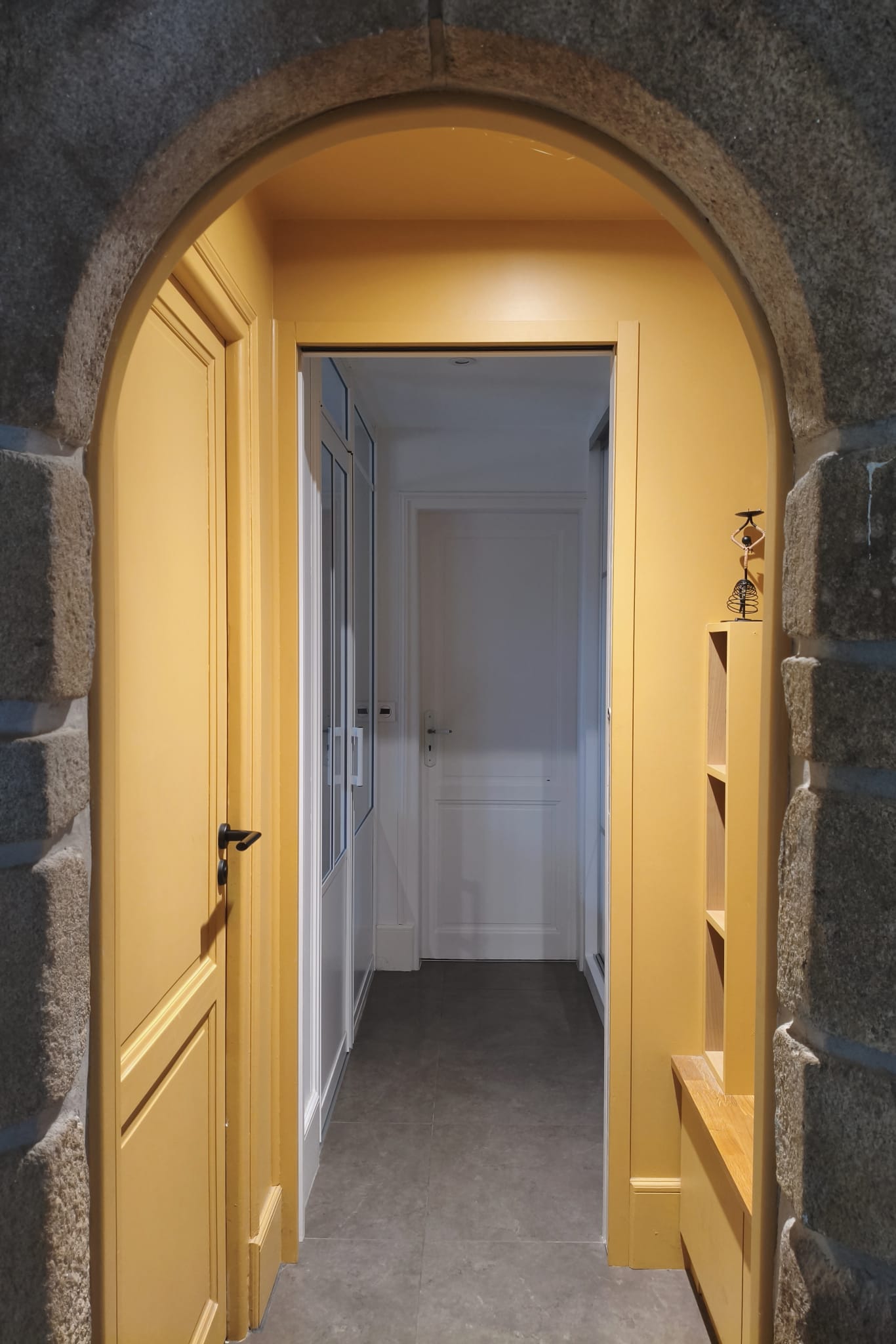Porte et murs ocre du sas d'entrée derrière l'arche en pierre, couloir en enfilade