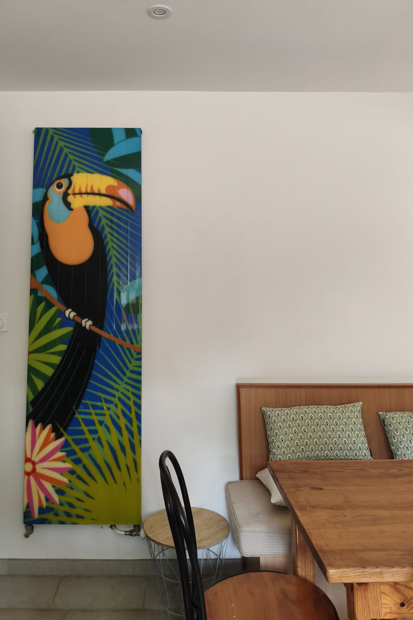 Coin repas : banquette, table en bois et panneau décoratif au toucan