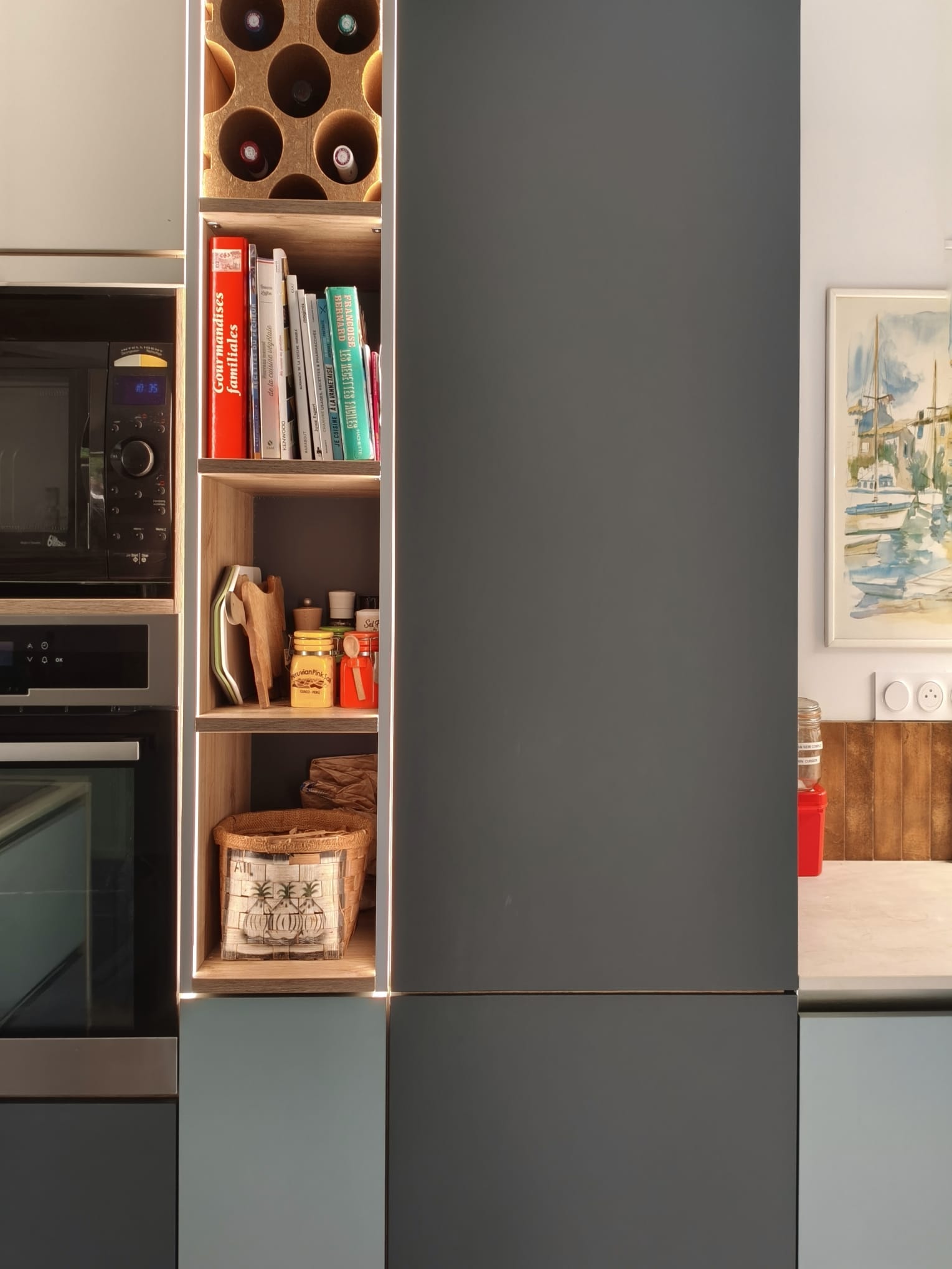Niche en bois entre les colonnes : range-bouteilles, livres de cuisine et paniers