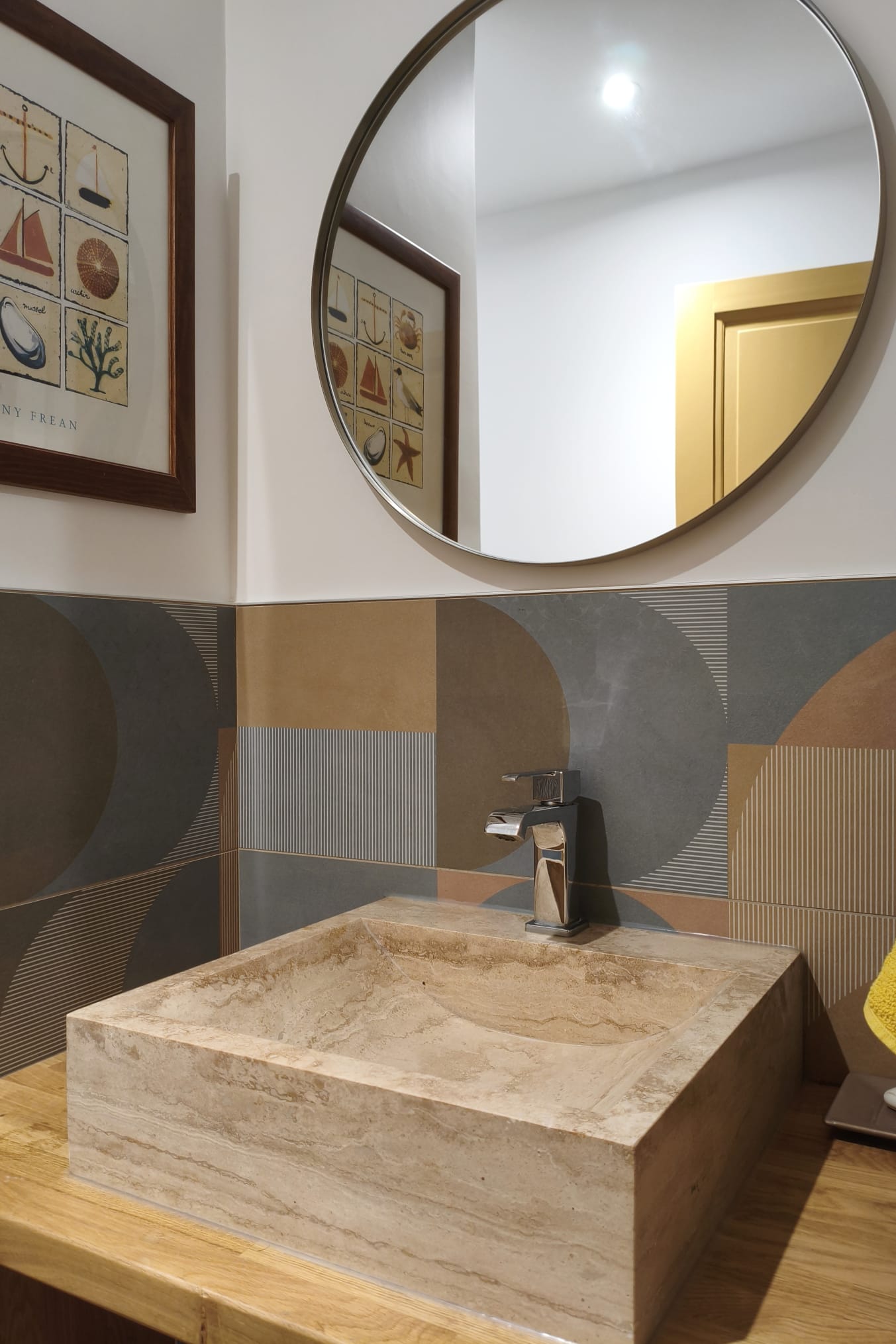 Lave-mains en pierre sur un plan en bois, miroir rond et faïence colorée