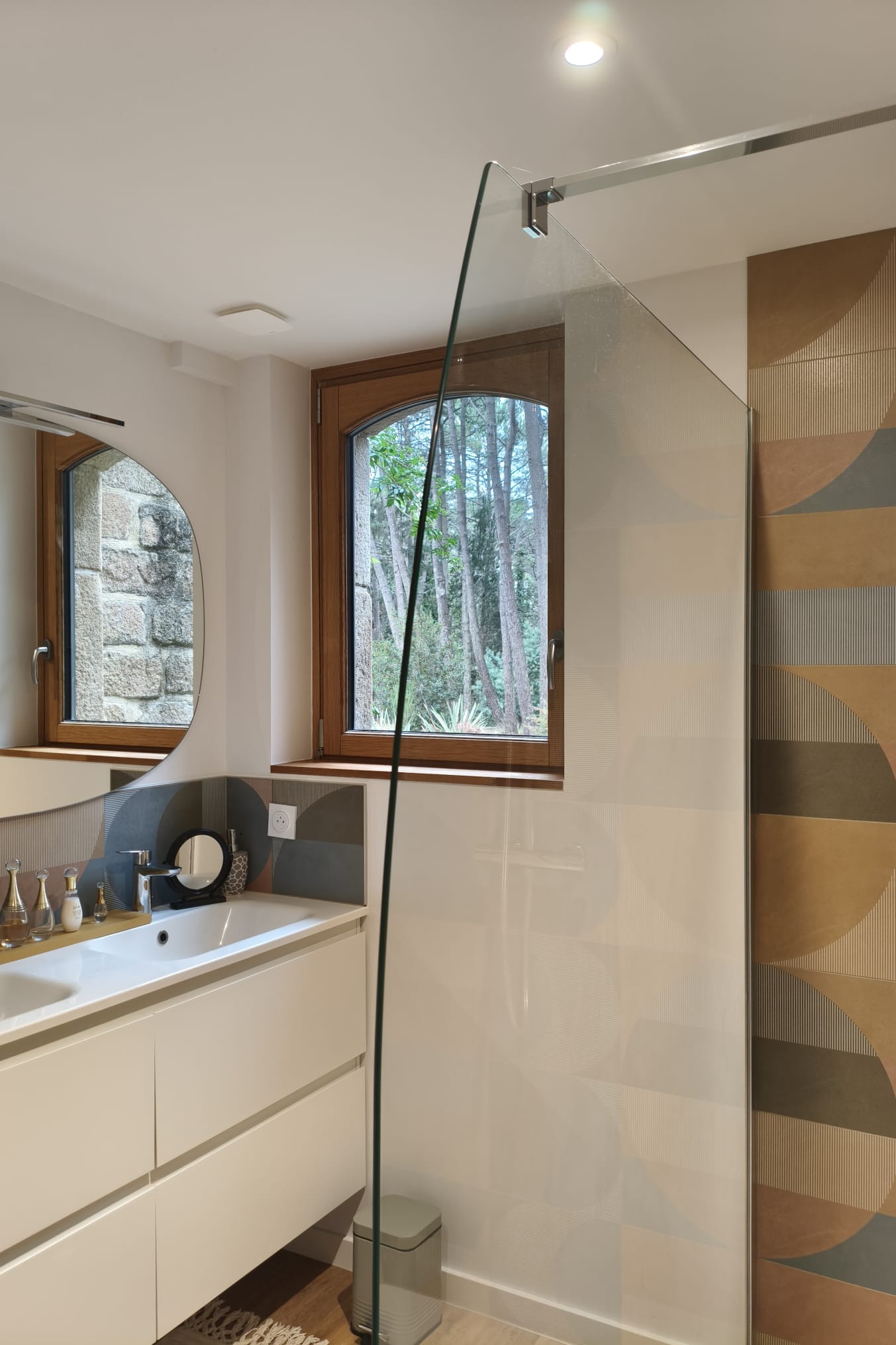 Salle de bains : meuble vasque blanc, fenêtres cintrées et paroi de douche en verre