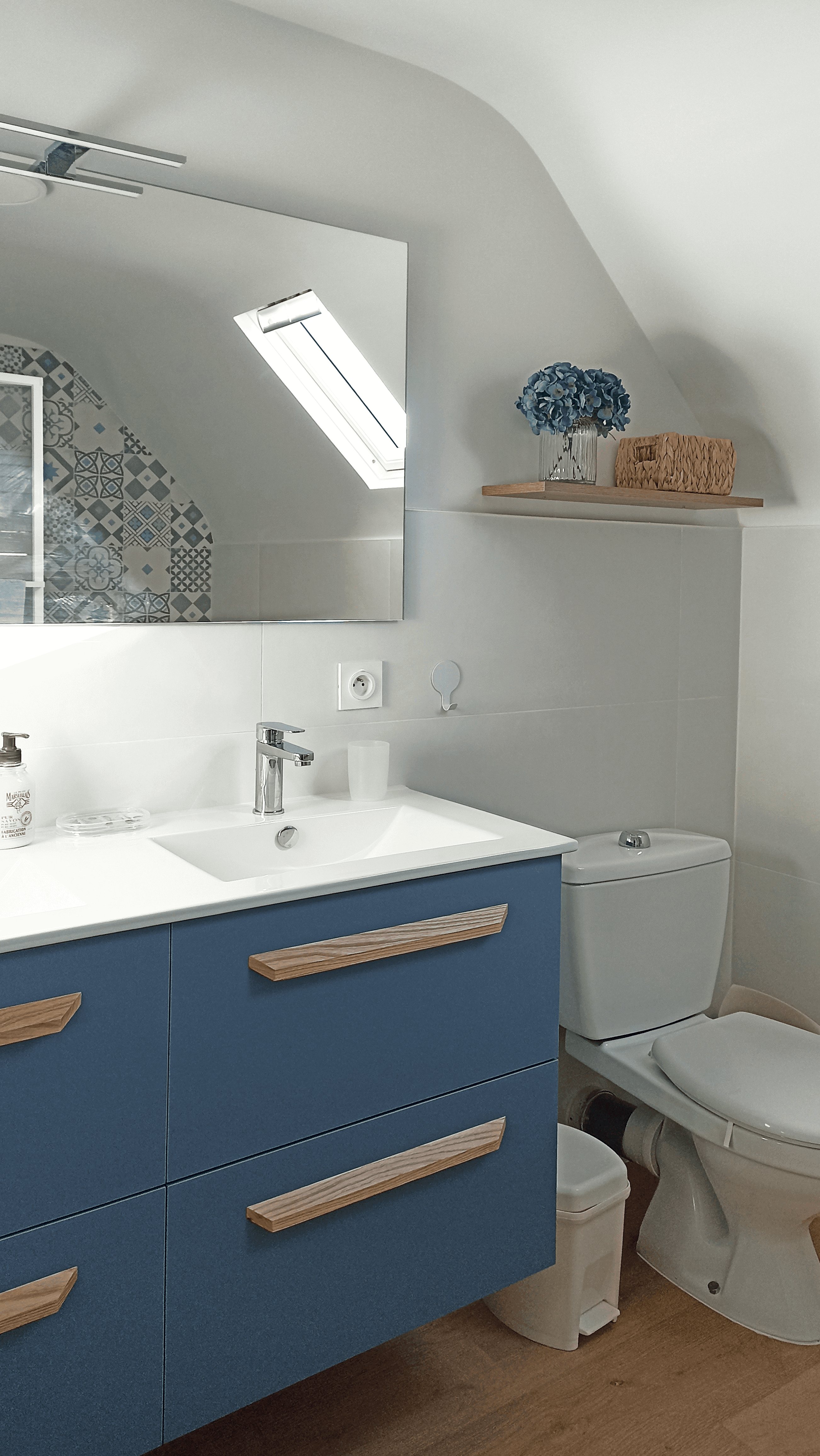 Salle de bain rafraîchie sous rampant : meuble vasque bleu, poignées en bois et velux